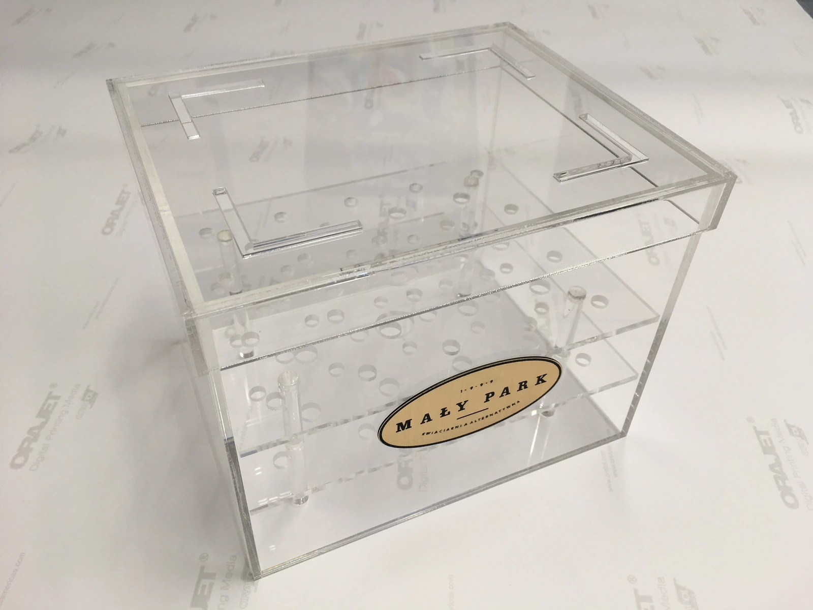 Maly Park — Transparent multi-level acrylic showcase with a wooden logo on the front, intended for presenting collections