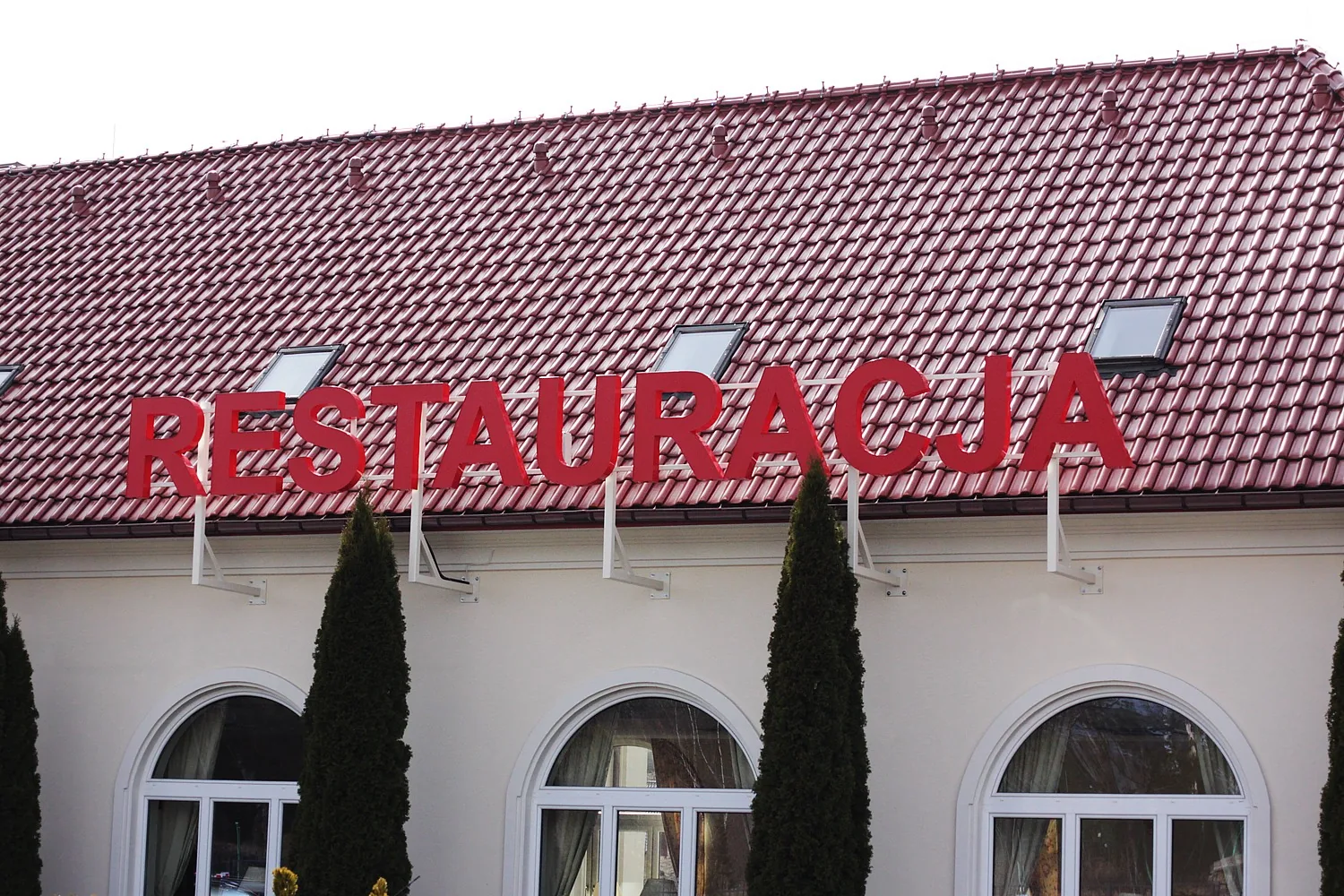 RESTAURACJA — Lightbox light from red lettering for white facade budynku from red dachem.